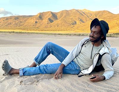 student lying in sand with mountains in back